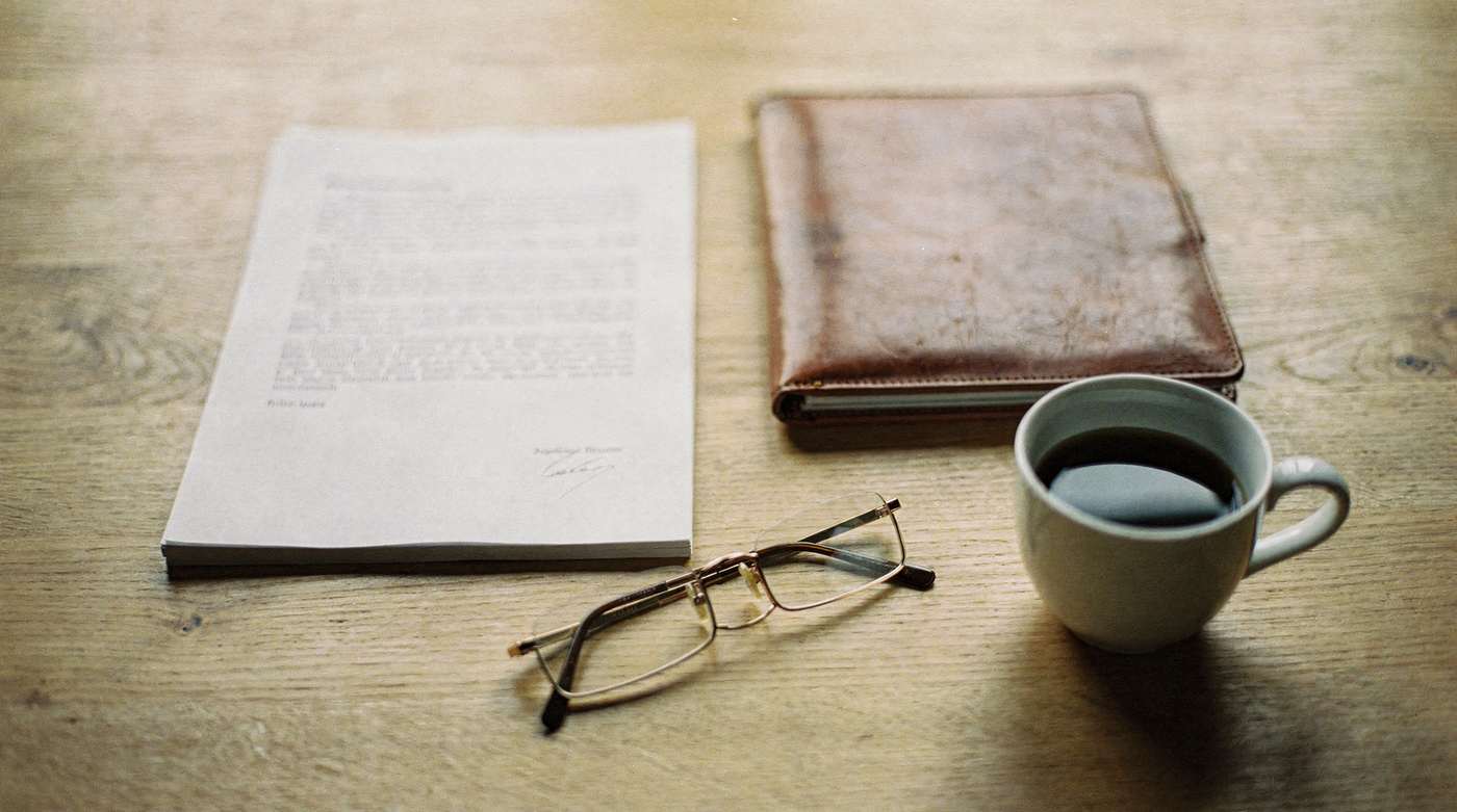 A printed statement, reading glasses and a cup of coffee on a desk